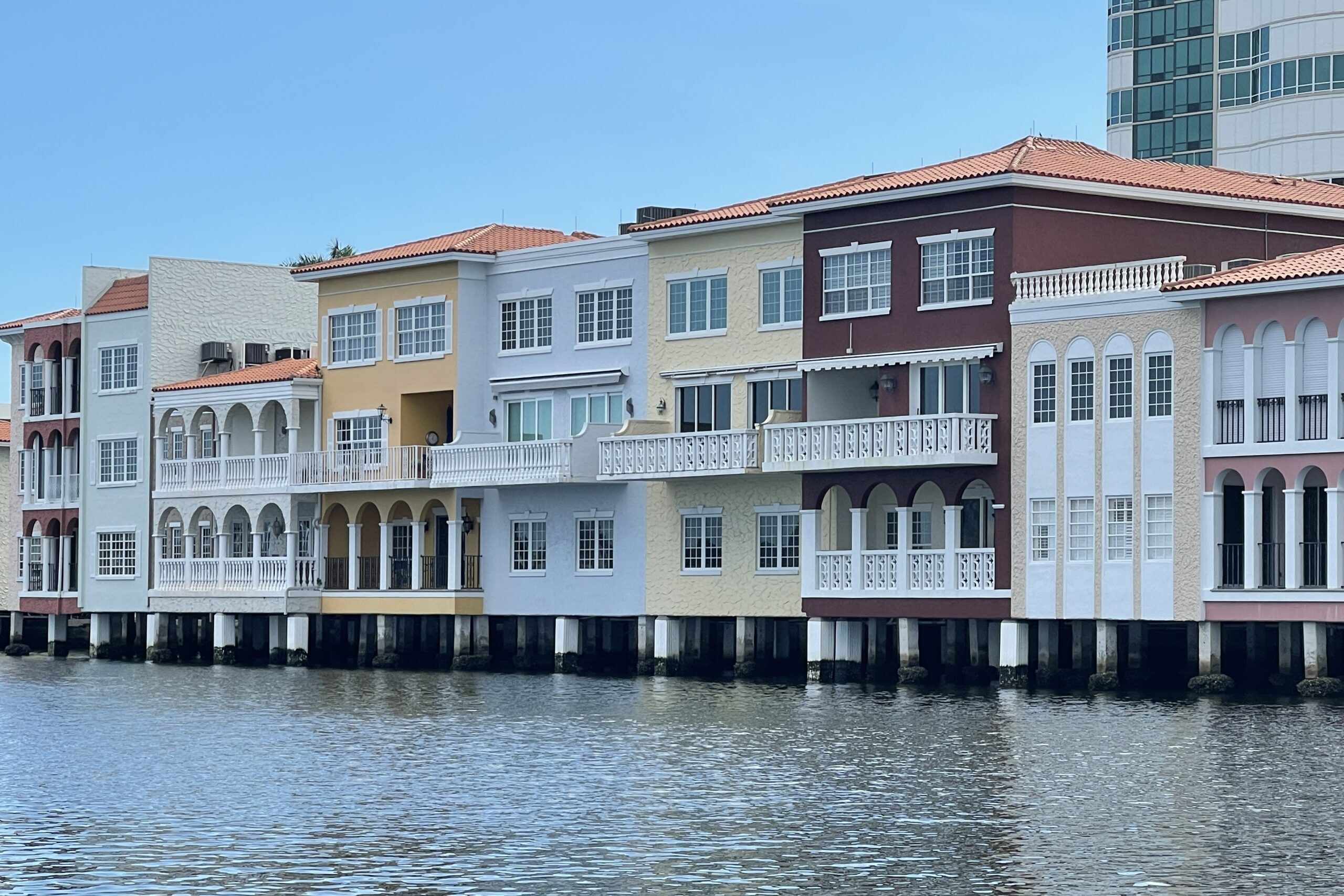 Canal-Side Color – Waterfront Living in Style Row of colorful Mediterranean-style waterfront homes with balconies overlooking a calm canal in Naples, Florida.