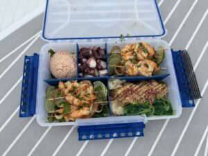 Coastal Gourmet in a Box Waterproof tackle box on a boat table filled with grilled shrimp, ahi tuna, crab salad, and octopus