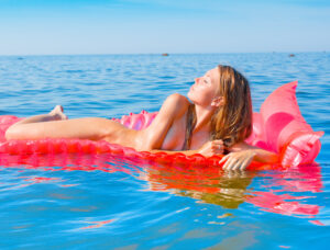 Bare to Be Free – Float Into You Woman floating nude on the water, eyes closed, embracing coastal freedom and natural beauty.