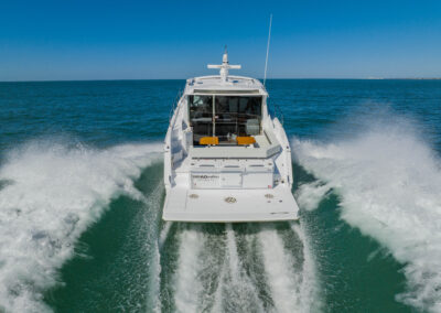 BRADventures yacht viewed from behind, cruising at high speed with a wide wake and logo in view