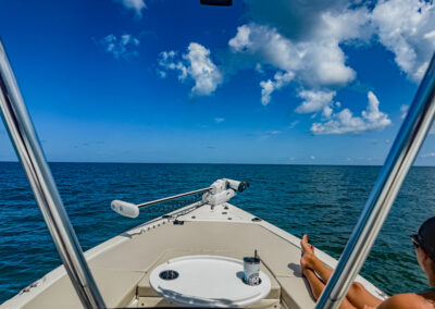 Person lounging at the bow of a boat with a drink, cruising on calm blue Gulf waters under a partly cloudy sky