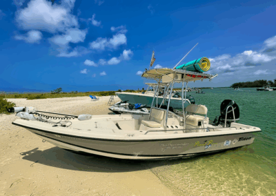 Center console boat parked on a beach with a rolled float strapped to the top and chairs in the background